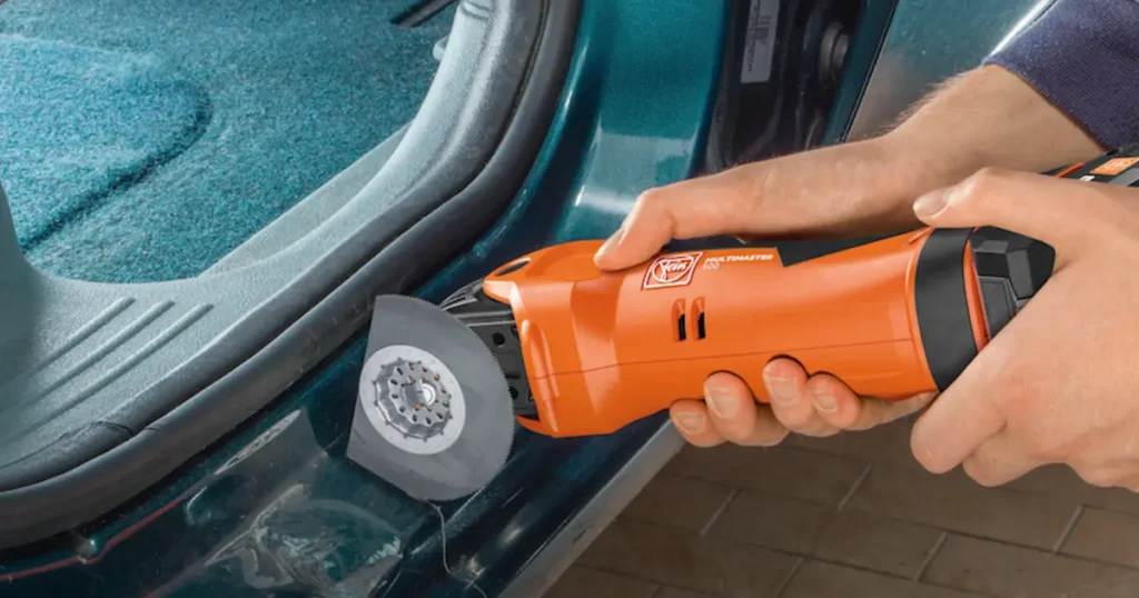 Hands operating an orange Fein MultiMaster oscillating tool with a segment blade, making a precise cut along the interior floor edge of a vehicle.