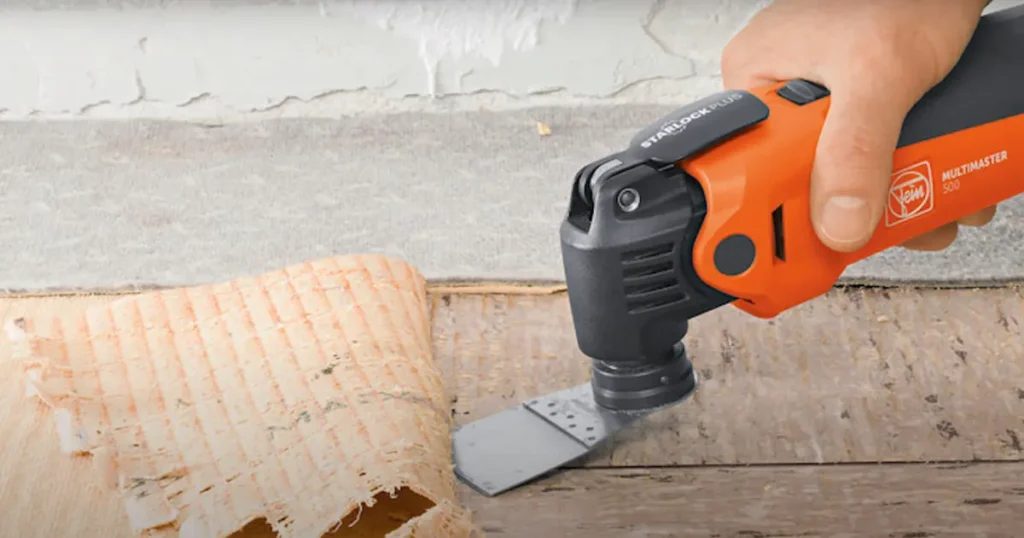 Fein MultiMaster StarlockPlus oscillating tool using a rigid scraper blade attachment to remove old material from a wooden surface.