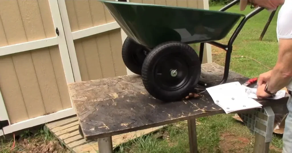Dual Wheel Wheelbarrow assembly on a wooden table with parts and instructions