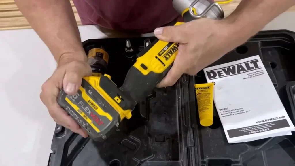 A person's hands are attaching a yellow DEWALT 20V MAX battery to the DEWALT PEX Expander DCE400D2 tool, with the kit box in the background.