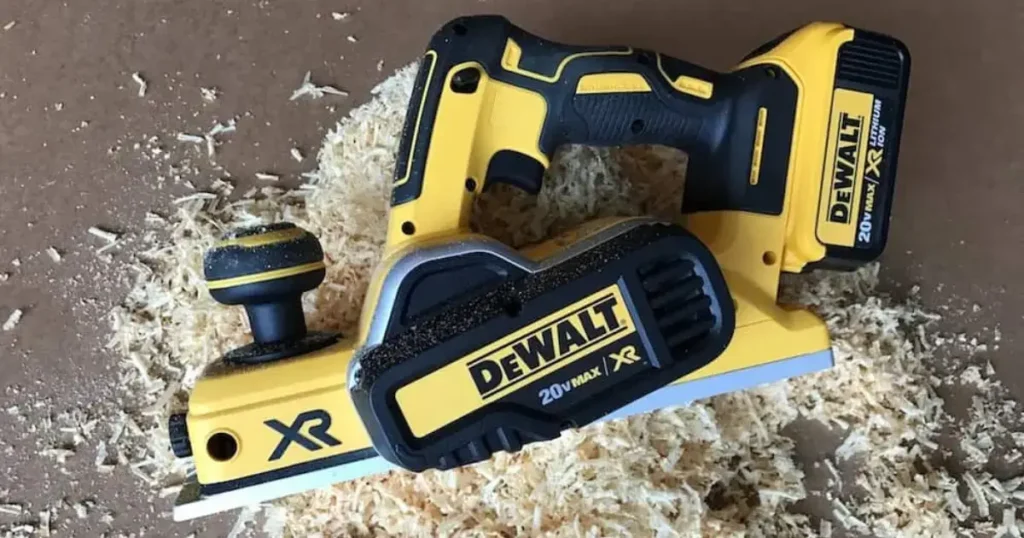 The DEWALT 20V MAX Cordless Planer (DCP580B) with battery attached, resting on a pile of fresh wood shavings it produced, showcasing its planing efficiency.
