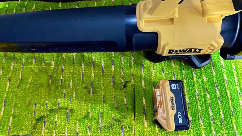 A close-up of the DEWALT DCBL722B blower's nozzle next to a DEWALT 20V MAX 8Ah battery, showing battery compatibility.