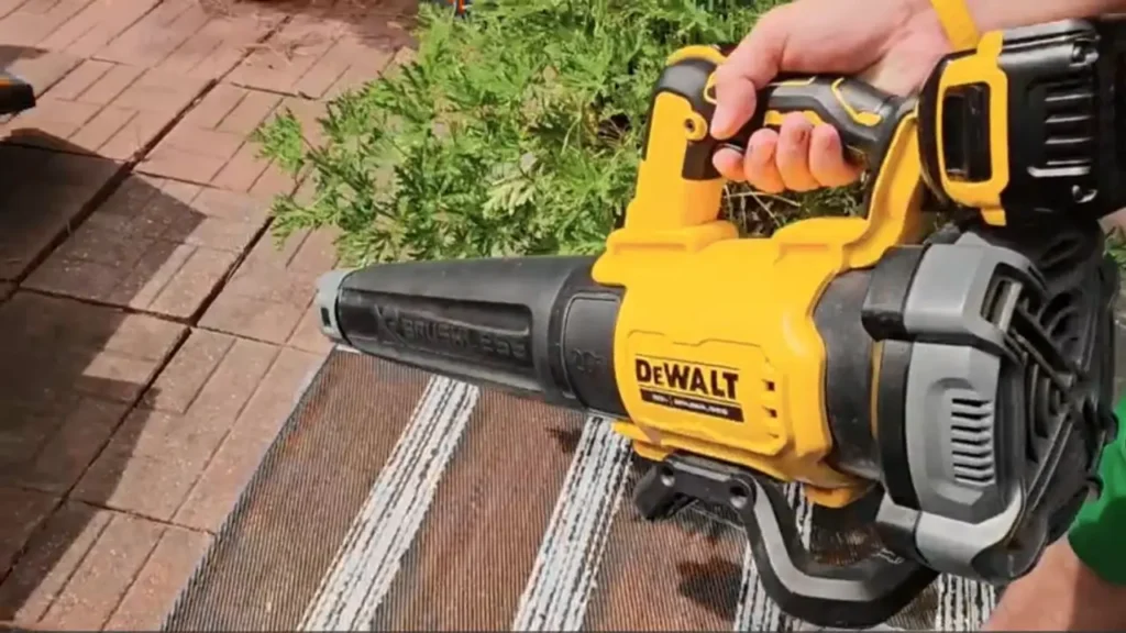 A person holding and operating the DEWALT DCBL722B cordless blower on a tiled patio, demonstrating its handling and design.