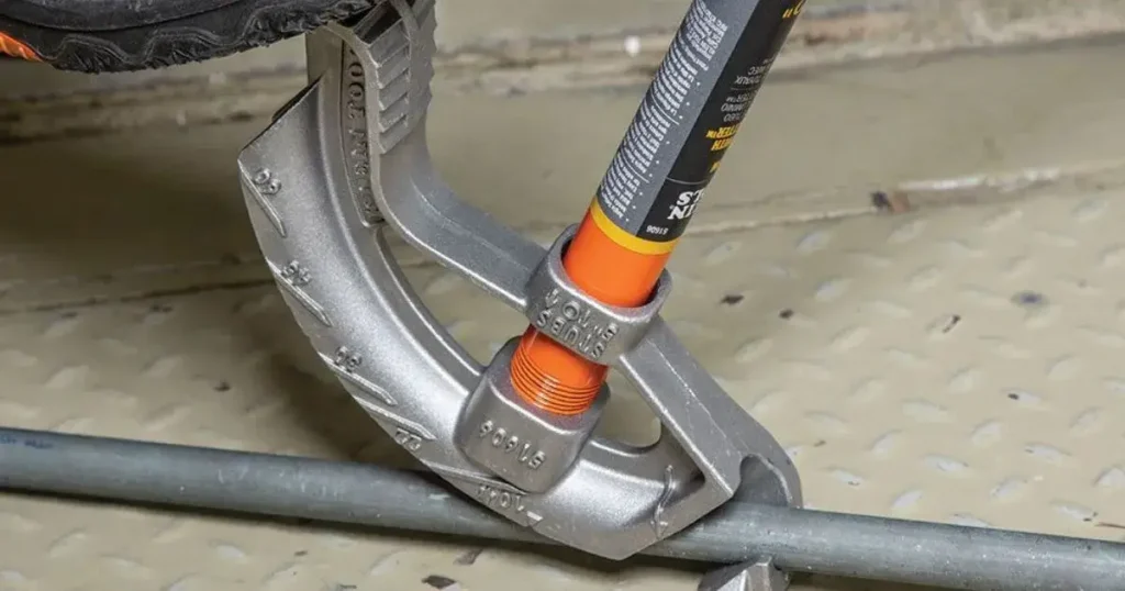 A close-up view of the Klein Tools 51607 conduit bender with a foot pressing down on its wide, grooved foot pedal while bending a metal conduit, showcasing the clear angle markings and stability during use.