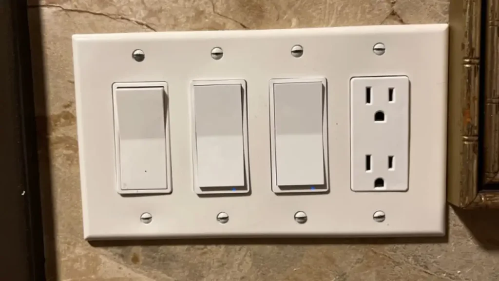 A white multi-gang wall plate featuring three modern paddle-style smart light switches and one electrical outlet.