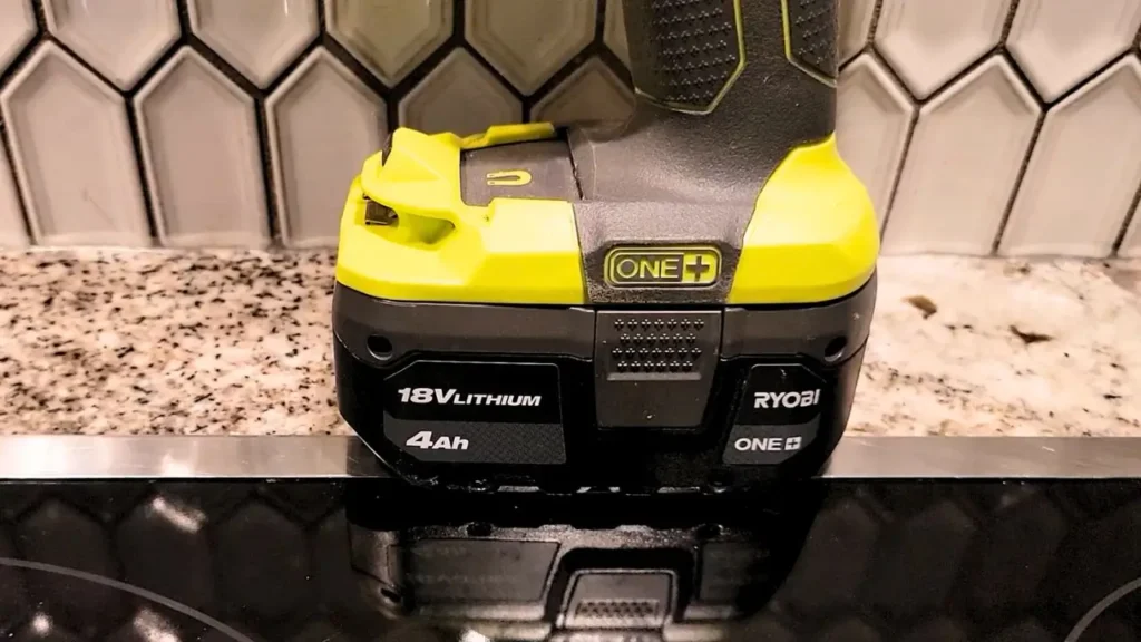 Smart AI Gears: Close-up shot of the 18V Lithium 4Ah Ryobi ONE+ battery attached to a Ryobi hammer drill, showing the ONE+ branding and battery voltage. Placed on a dark, reflective surface with white tiles behind it.
