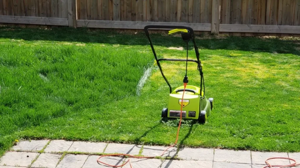 The Sun Joe MJ401E mower with its orange extension cord laid out on a patio and lawn, showing how a corded mower works.