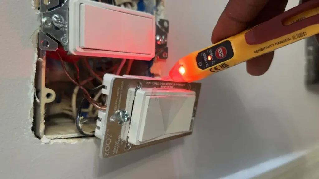 A hand holding a glowing voltage tester near a Zooz Z-Wave Dimmer during installation, showing a live wire warning.