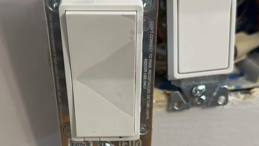 A close-up of the side of a Zooz Z-Wave Dimmer during installation, revealing warning labels and its slim design.