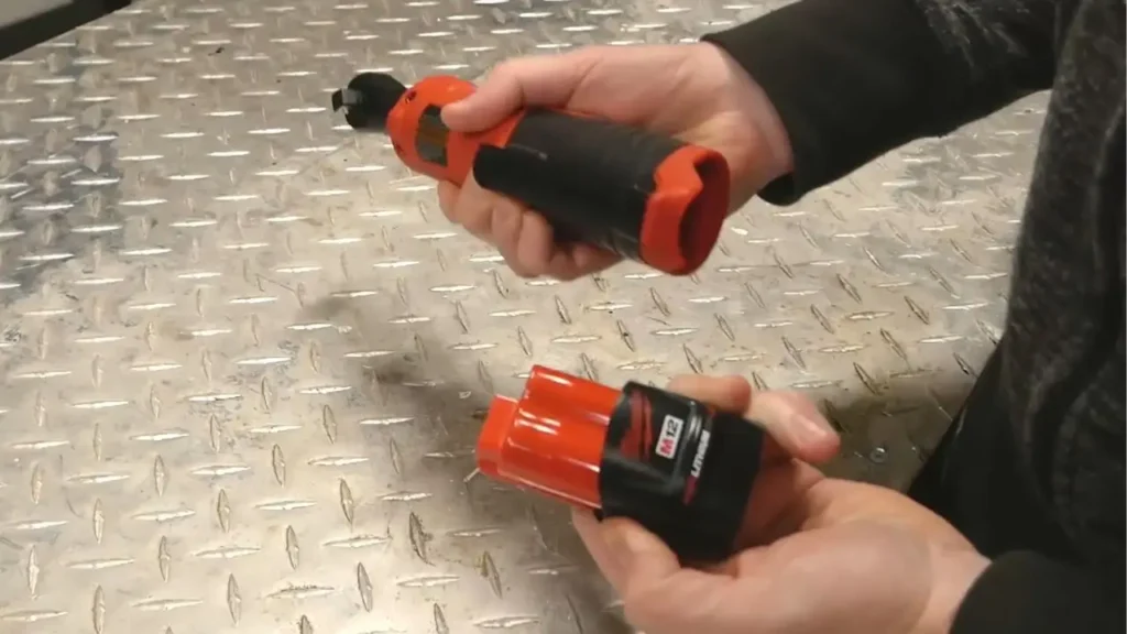 Hands attaching Milwaukee M12 battery to cordless ratchet