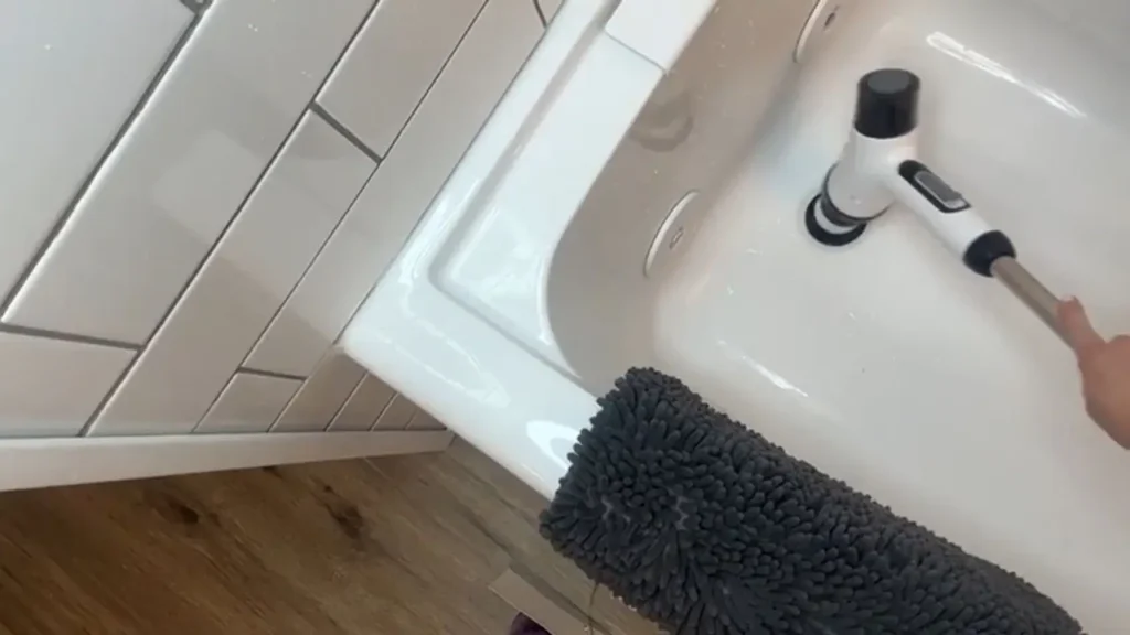 The electric spin scrubber cleaning the grout and tiles around the bathtub, showing its effectiveness on bathroom surfaces.