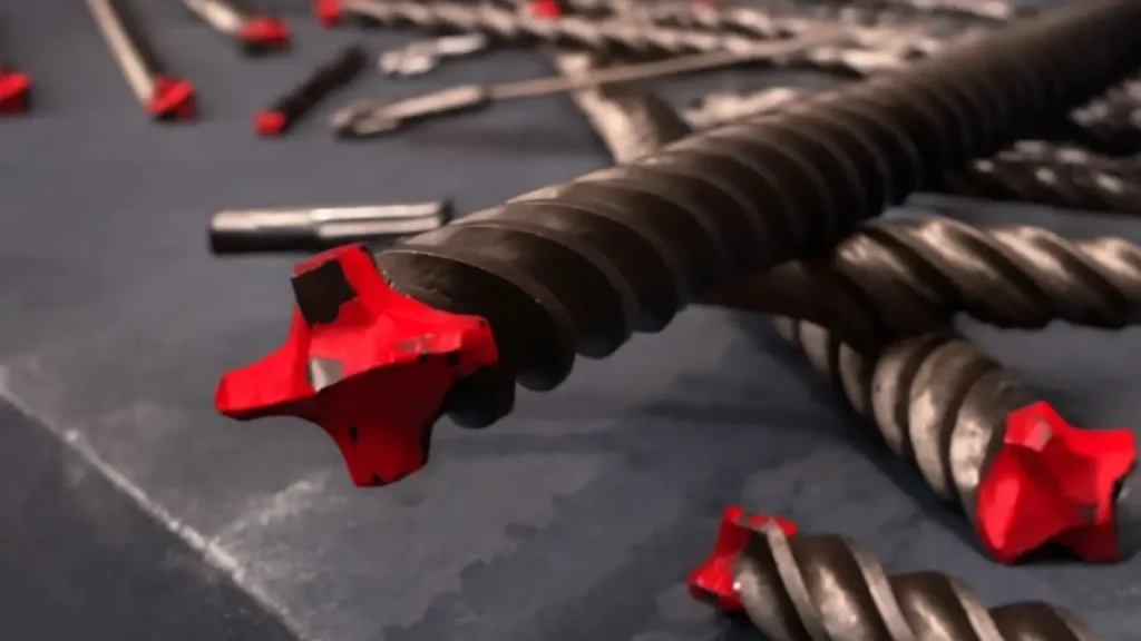 Masonry drill bits with sharp red carbide tips arranged on a surface, showcasing the precision and durability for tough drilling tasks.