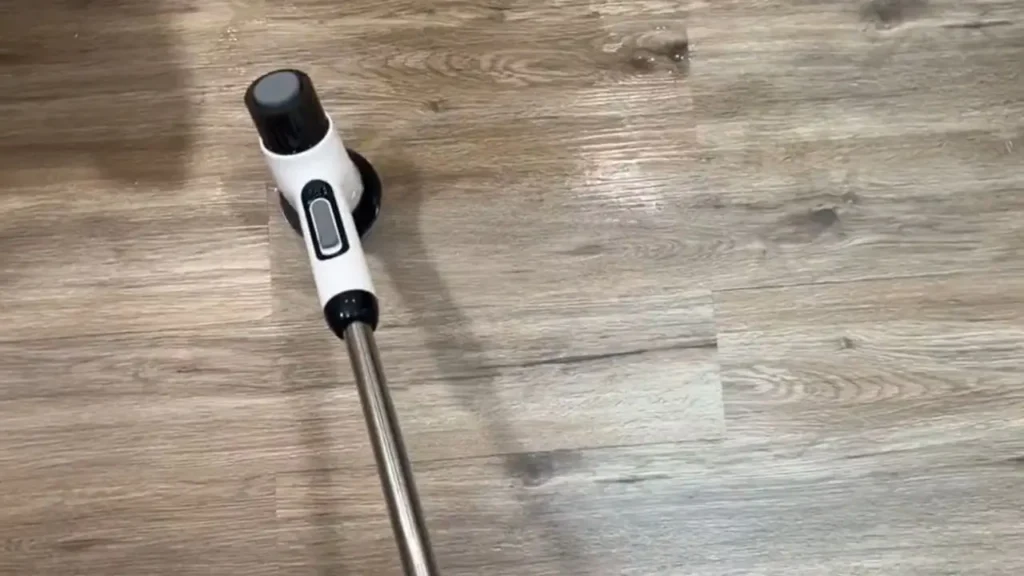 The electric spin scrubber on the floor with its extended handle, designed to make cleaning large areas easier.