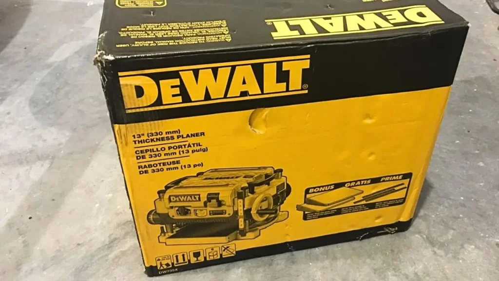 The yellow and black retail box of the DEWALT DW735X 13-inch thickness planer, showing the product and mentioning the included bonus accessories.