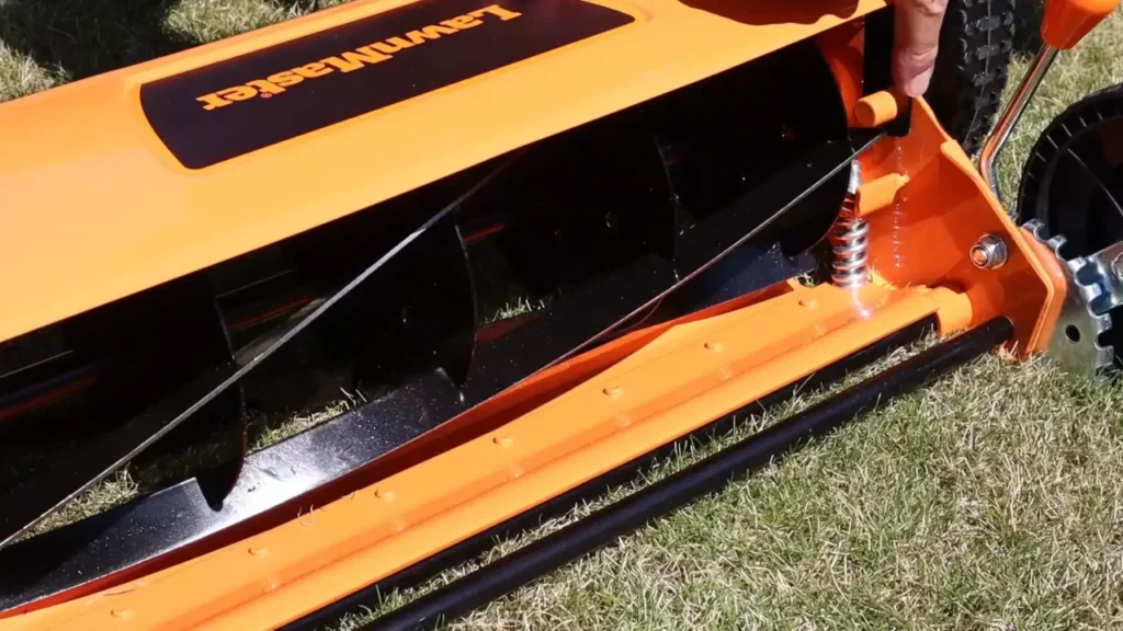 A close-up of the metal blades and roller on the bottom of a manual push mower.