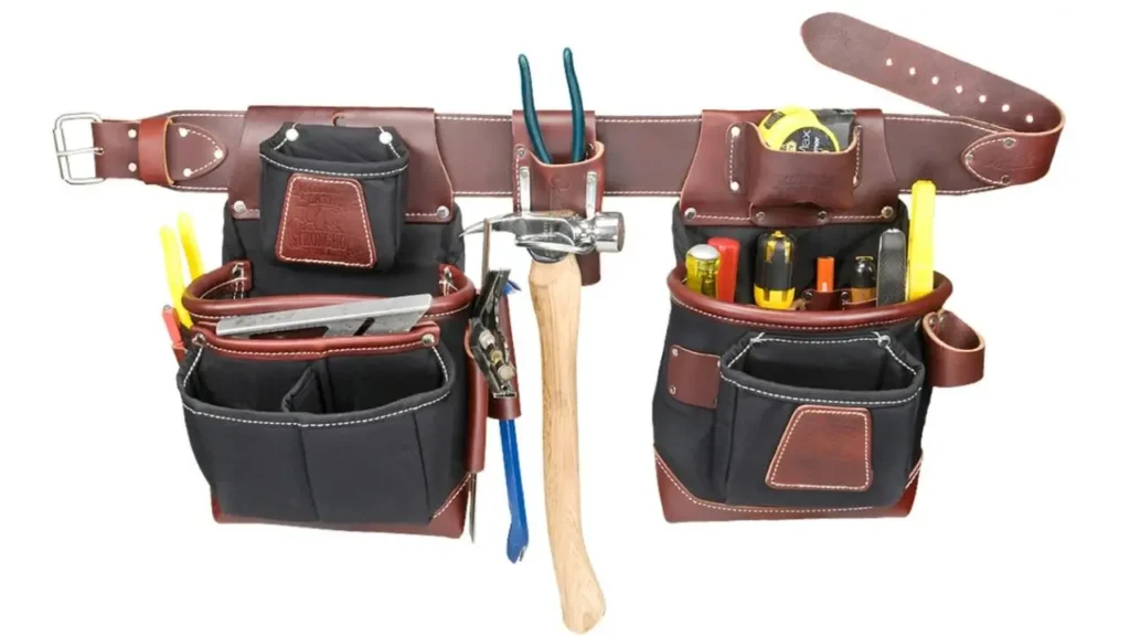 A heavy-duty leather and canvas tool belt with multiple pouches and pockets, holding various construction tools like a hammer, tape measure, pliers, and screwdrivers. The belt is dark brown leather with black pouches.