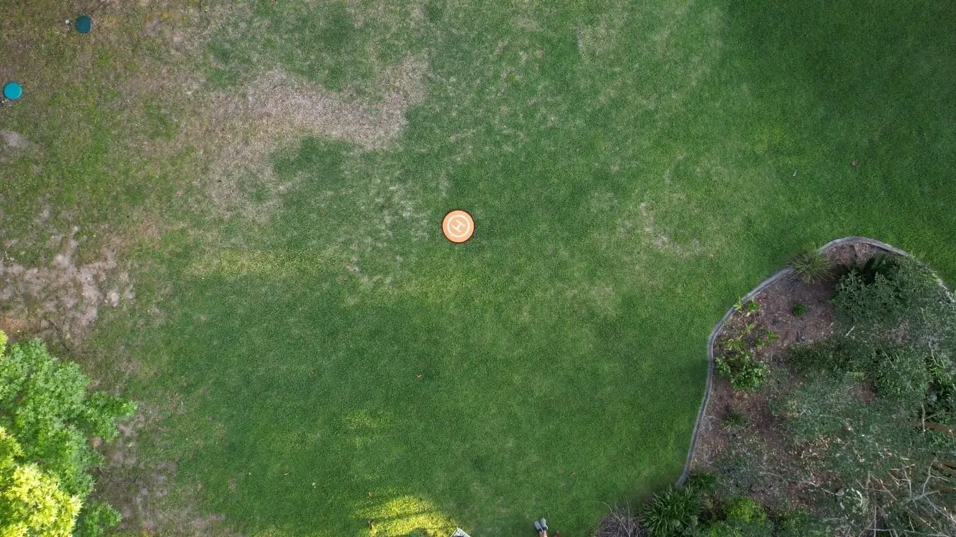 An aerial shot of an orange landing pad placed on a green lawn, showing its high visibility from a drone's perspective.