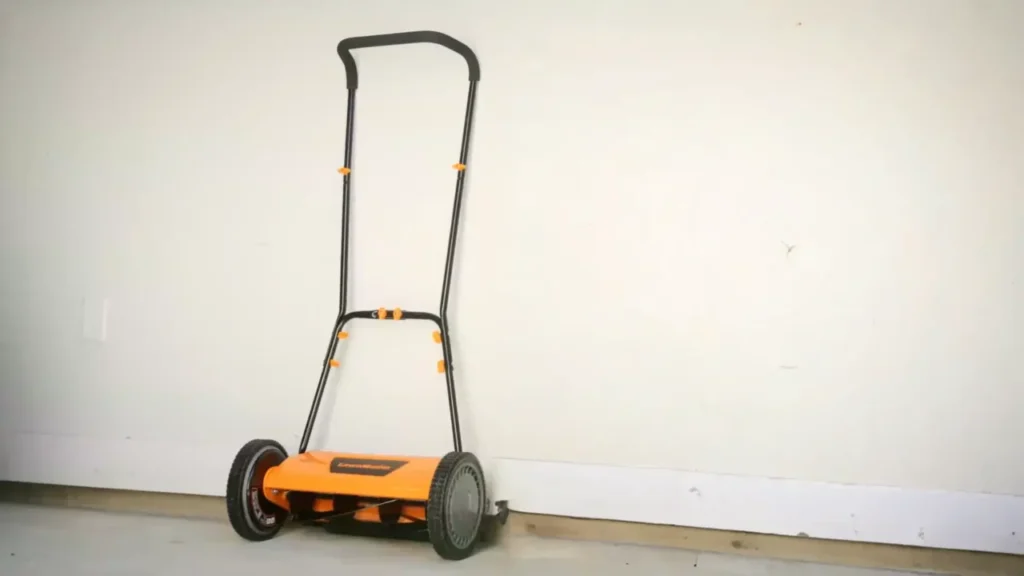 A manual push mower is stored vertically in a garage to save space.