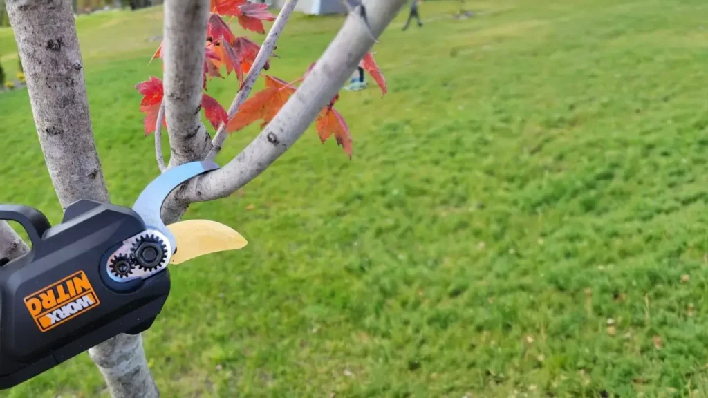 A Worx WG330 cordless pruner cutting a branch, with its titanium-coated blade in action.