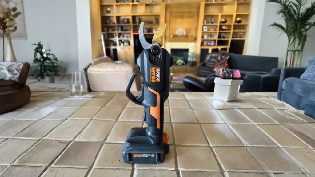 The Worx WG330 20V Nitro pruner stands upright on a tiled floor, with a living room in the background.