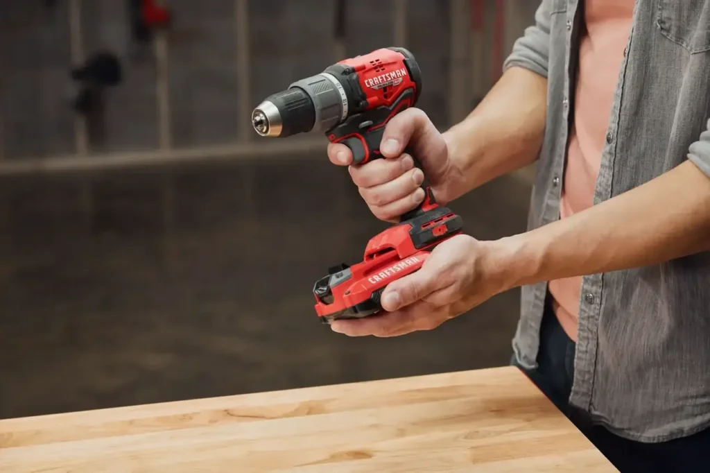 A user holding the Craftsman CMCD713C2 V20 cordless drill over a wooden surface.