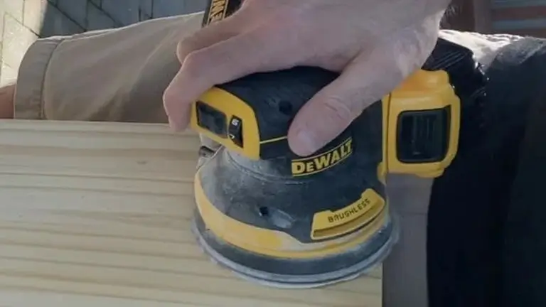 A person's hand using the DEWALT DCW210B sander on a smooth wooden board.