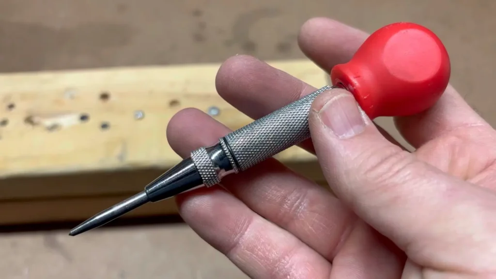 A close-up view of the NEIKO 02638A Automatic Center Punch being used by a metalworker to create a precise mark on a wood plank. This detailed review on Smart AI Gears covers how this tool helps with accuracy in metalworking.
