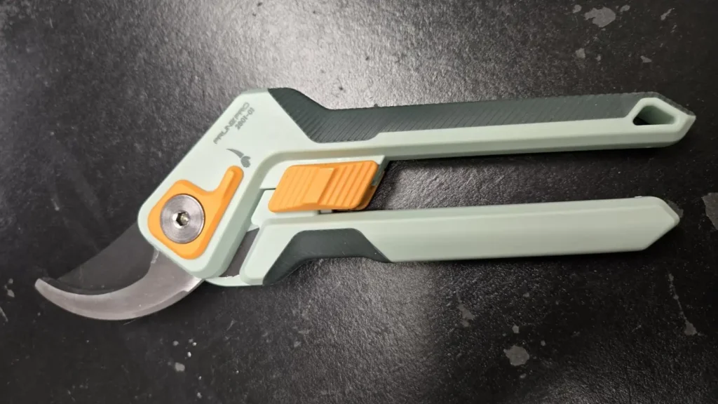 A close-up of the PrunePro pruning shears, focusing on the high-tension spring and the anti-break lock system.