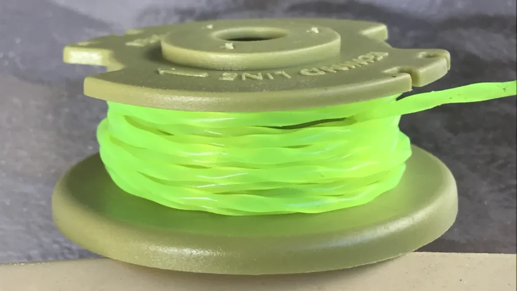 Three bright green trimmer line spools stacked in a triangle on a wooden surface with a cordless grass trimmer in a blurred background.