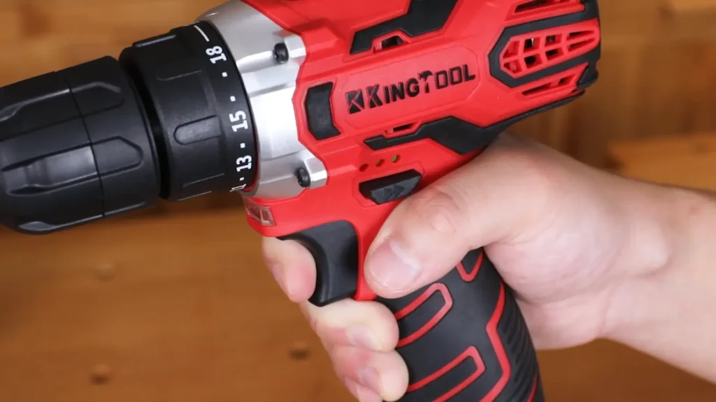 A close-up view of a hand gripping a red power drill, focusing on the trigger, forward/reverse switch, and adjustable torque collar.
