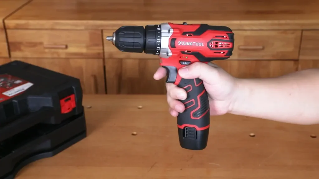 A person holding a red and black 12V cordless power drill, demonstrating its compact size and ergonomic grip.