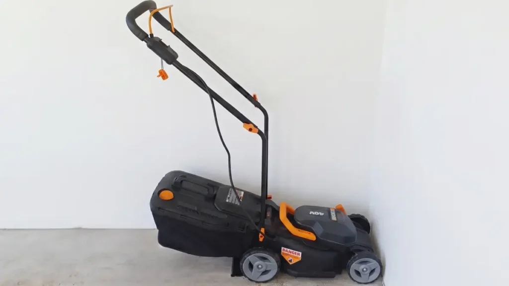 A black and orange WORX 40V cordless lawn mower with an attached black grass collection bag, sitting on a flat surface against a plain white wall.