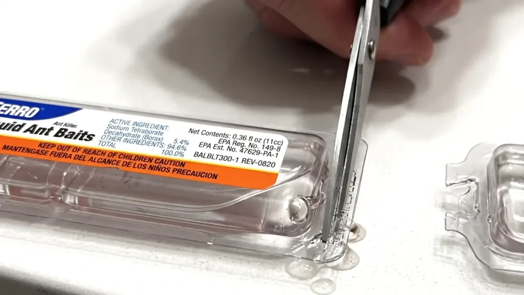 Close-up of cutting the plastic tab of a TERRO Liquid Ant Bait station using scissors to avoid spills.