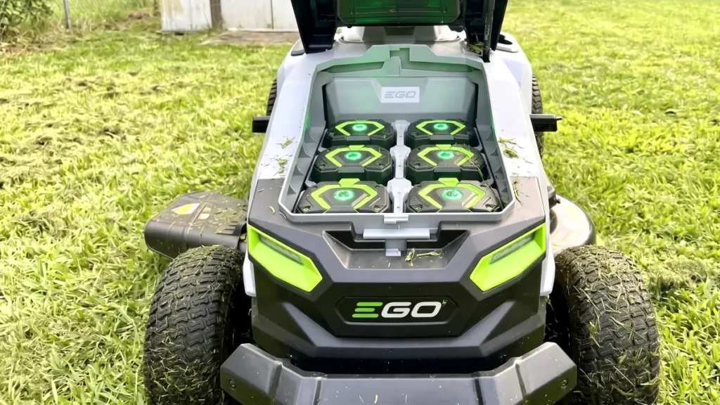 Six lithium batteries sitting inside the open battery compartment of a lawn tractor.
