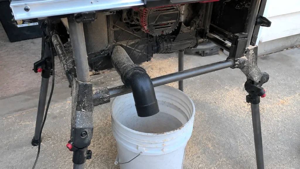 Back view of the table saw dust port shooting wood dust into a 5-gallon plastic bucket.
