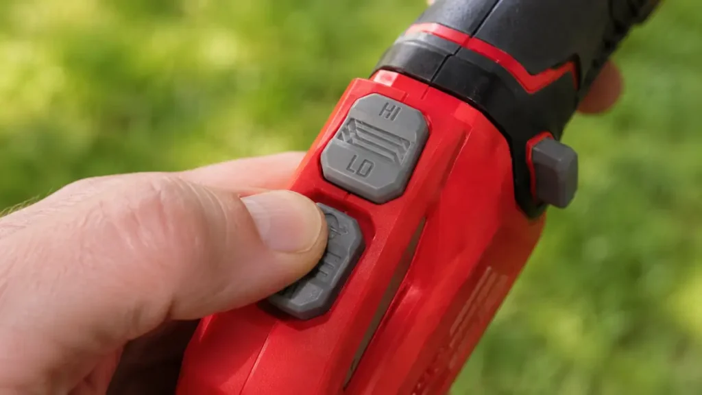 Hand pressing the line-feed button on the handle of a red string trimmer.