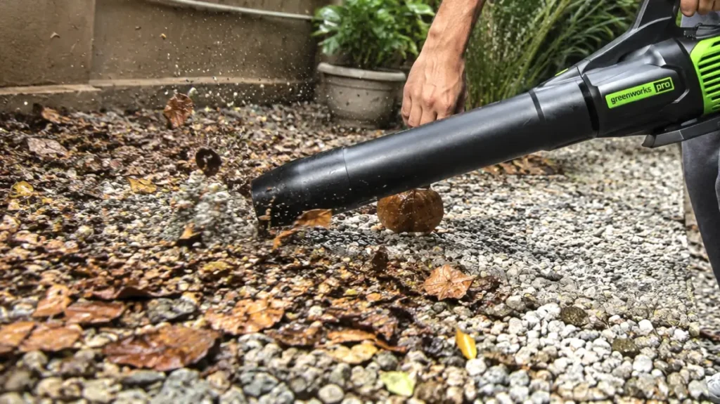 Close-up of a leaf blower nozzle held near gravel to lift wet leaves.