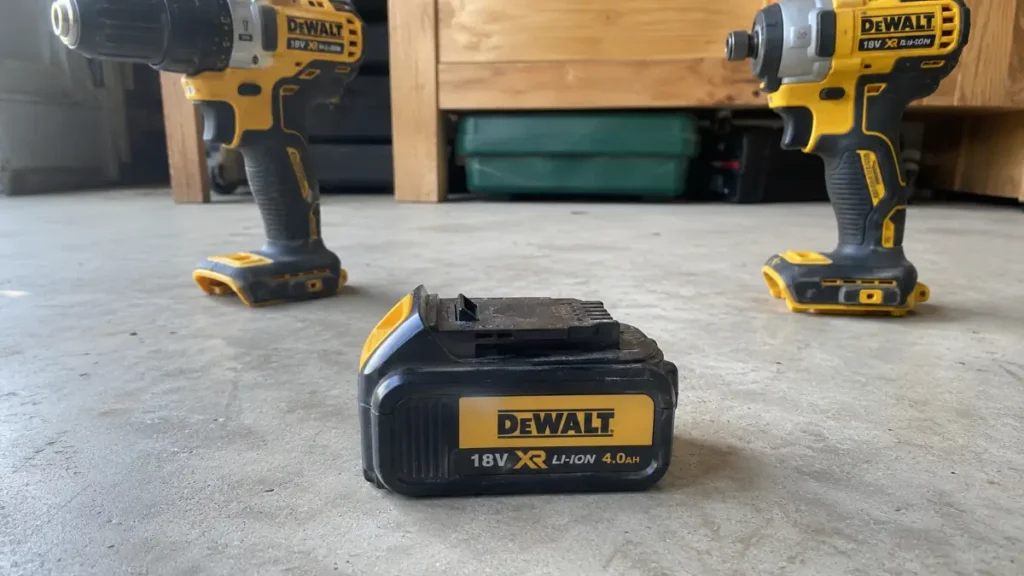 A single cordless tool battery pack sitting between two compatible bare tools from the same brand ecosystem.